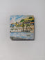 A square wooden magnet on a white metal background featuring the Charlestown watercolour print by R Singleton - reproduced with printing by HLSdesigner in Cornwall. Featuring the tall ship that frequents in the bay of Charlestown , views from the railings the opposite side of the bay - with the fishing village seen in the back ground, painted using colour washes and negative space. 