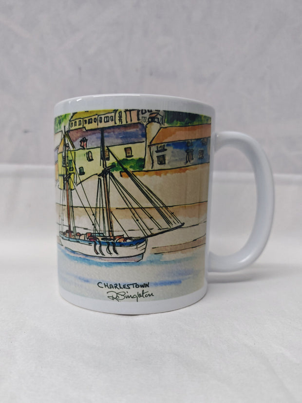 A white ceramic mug featuring a full wrap around print of the Charlestown harbour watercolour painting by R Singleton - reproduced in tribute by HLSdesigner, displaying the tall ship that comes in to moor at the quay wall where the village of old fishing houses overlook the quay. Cornwall coastal scenes 