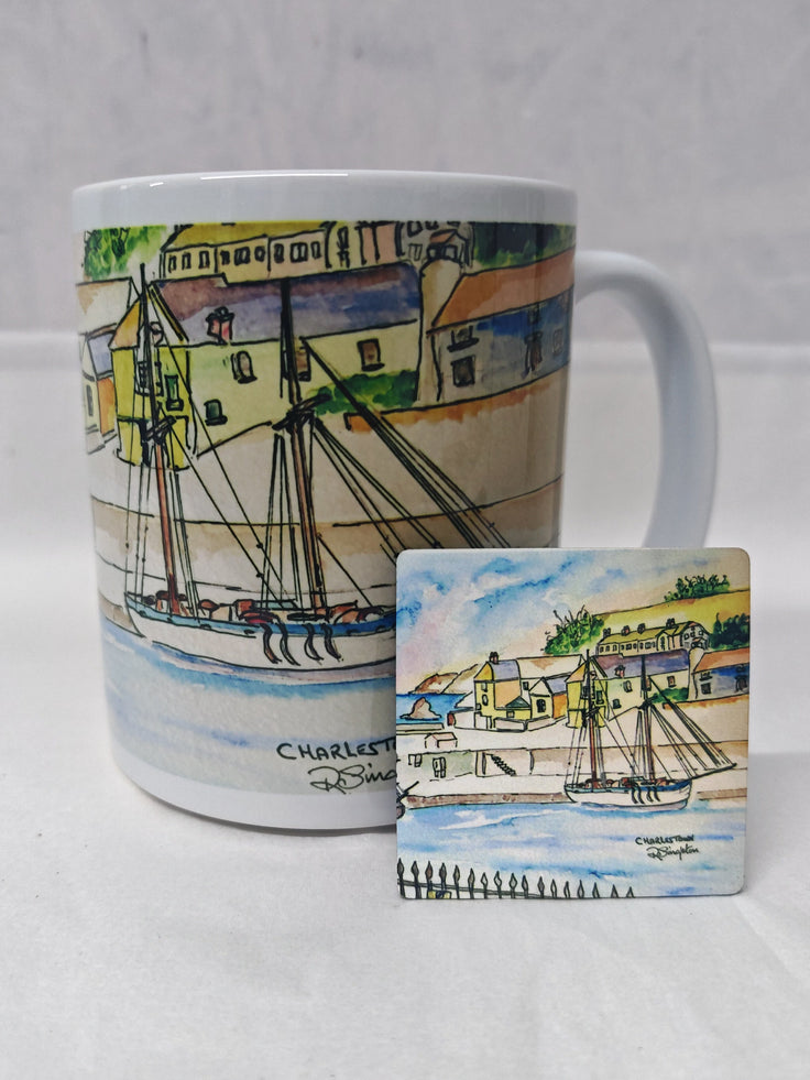 A white ceramic mug with a colorful watercolor illustration of a harbor scene with boats and buildings, shown alongside a matching square coaster on a light gray fabric background. Watercolour painting by R Singleton showcasing the Charlestown fine art print reproduced on a ceramic mug alongside a matching magnet next to it