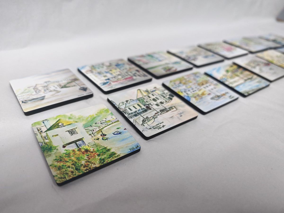 A set of square coasters with colourful coastal and harbour illustrations, arranged in a row on a light grey fabric background. Cornwall coastal scenes in watercolour by R Singleton reproduced exclusively by HLSdesigner into lovely collectable magnets, featuring the old watch house, Polperro, Sennen cove and more 