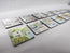 A set of square coasters with colourful coastal and harbour illustrations, arranged in a row on a light grey fabric background. Cornwall coastal scenes in watercolour by R Singleton reproduced exclusively by HLSdesigner into lovely collectable magnets, featuring the old watch house, Polperro, Sennen cove and more 