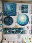A gallery-style wall display featuring multiple ocean-wave themed artworks, including several square and circular paintings in swirling blue, teal, and white tones, with small framed labels and a 'No AI Art' sign nearby. All of my work is painted and designed by me, Hannah Singleton at HLSdesigner in Cornwall. Featuring ‘a drop in the ocean’ original oil painting inspired by close up viewpoints of the ocean.