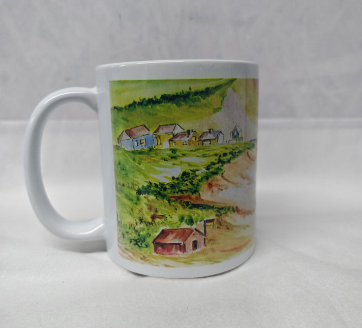 A white ceramic mug featuring a printed landscape illustration of a small village with green hills, trees, and houses, set against a light Gray textured background. This is the side of the Mawgan Porth beach painting in watercolour by R Singleton - reproduced onto a mug and other accessories exclusive to HLSdesigner in Cornwall. Coastal seascape beach paintings 