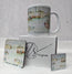 A white ceramic mug and two matching square coasters printed with a watercolour Newquay Harbour scene, displayed with a branded white gift box on a white fabric surface. watercolour painting of Newquay harbour on a ceramic mug as well as a wooden coaster and magnet with hand printed mug box - painted by R Singleton Cornwall coastal scenes and reproduced by HLSdesigner