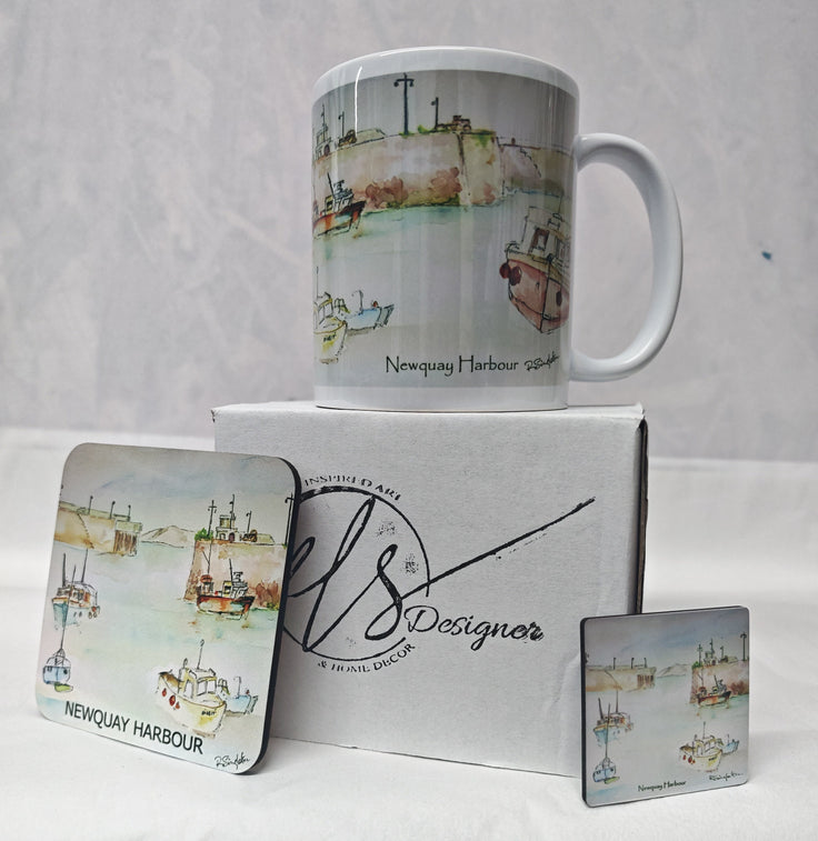 A white ceramic mug and two matching square coasters printed with a watercolour Newquay Harbour scene, displayed with a branded white gift box on a white fabric surface. watercolour painting of Newquay harbour on a ceramic mug as well as a wooden coaster and magnet with hand printed mug box - painted by R Singleton Cornwall coastal scenes and reproduced by HLSdesigner