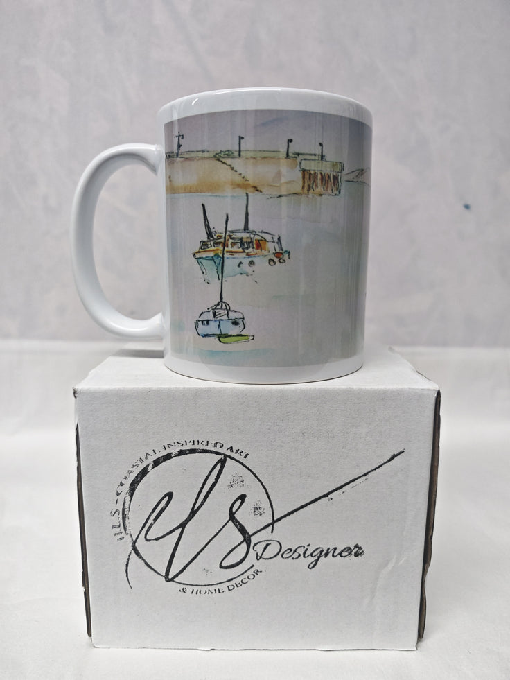 A white ceramic mug with a watercolour illustration of boats on water, displayed on top of its white branded box. HLSdesigner. painting by R Singleton as tribute printed onto mugs and accessories, Newquay Harbour Cornwall 