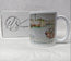 A white ceramic mug featuring a watercolour illustration of Newquay Harbour with boats and harbour quay walls, shown next to its white branded box. painting by R Singleton and reproduced onto mugs as tribute by HLSdesigner Cornwall