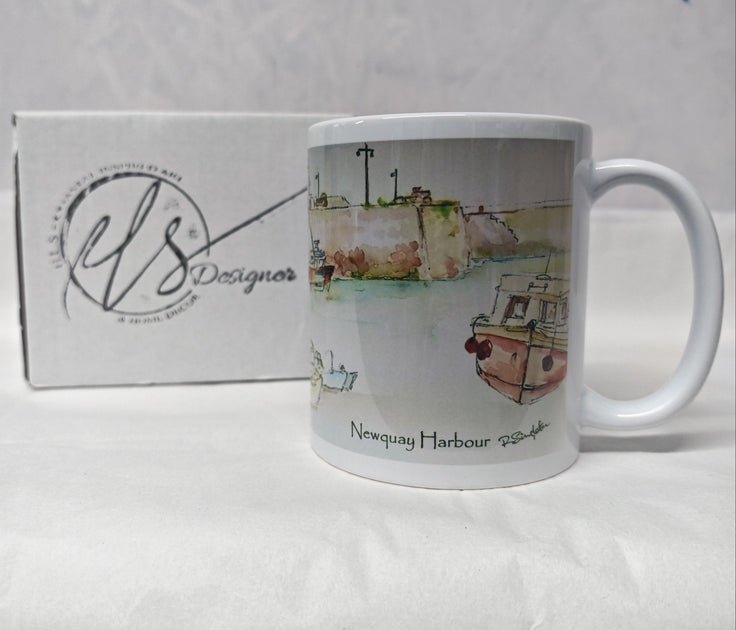 A white ceramic mug featuring a watercolour illustration of Newquay Harbour with boats and harbour quay walls, shown next to its white branded box. painting by R Singleton and reproduced onto mugs as tribute by HLSdesigner Cornwall