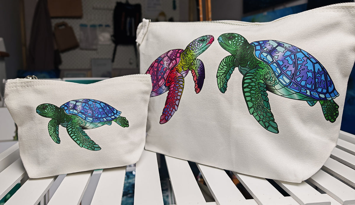 printed and designed in house, these accessory bags are sitting next to each other to compare in size, showing the turtle design collection. sitting on a white shelf with ocean art in the background