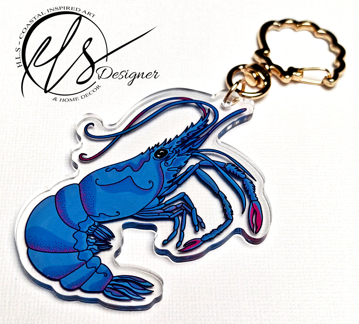 Blue king shrimp illustration designed by HLSdesigner featuring pink dotted shading techniques and blue hues throughout the drawing, printed onto clear shaped acrylic and finished with a metal gold seashell clasp and the HLSdesigner logo 