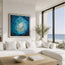Fish shoal 1 portrayed hung on a wall behind a large L-shaped sofa in a coastal beach house home with a coastal scene of a beach behind through the window. Print sizes are not to scale in this representation and vary in size options. Designed by Hannah Singleton at HLSdesigner - these prints feature abstract fish shoaling through the ocean in a vortex whirlpool motion. 