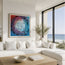 A framed abstract painting featuring a swirling vortex of blue, purple, and red with black fish-like shapes, displayed on a white wall above a modern white sectional sofa in a bright coastal living room.This is fish shoal 8 - a abstract collection of 12 pints featuring shoaling fish s you look up toward the surface. Designed by Hannah Singleton at HLSdesigner, coastal inspired art inspired by the ocean viewpoints.