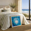 Framed fine art print featuring an abstract print of a under water vortex of moving ocean with fish swimming around and a brightly reflective center as they glide toward the surface. This print is by Hannah Singleton, fine artist from Cornwall and owner of HLSdesigner. Image shows this print leant against the end of a bed with a coastal each theme throughout 