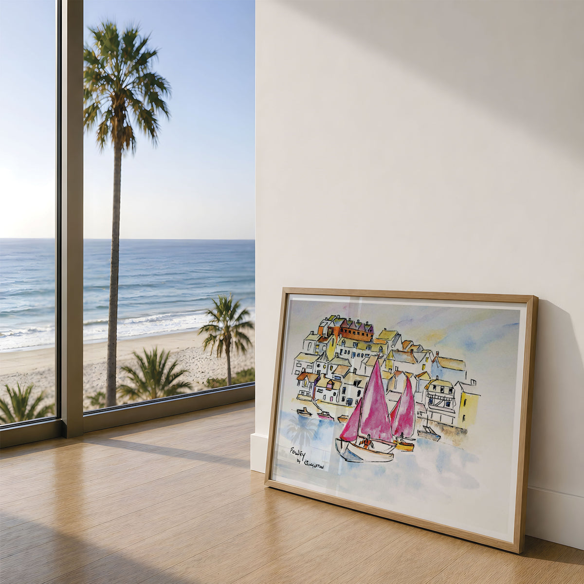 A framed watercolour painting of a coastal town with sailboats leans against a wall on a wooden floor, next to a large window showing a beach and ocean view with palm trees. This print is a reproduction of an original watercolour painting by Robert Singleton, Contemporary and modern with colour washes and use of negative space. His paintings depict the coastal town of Fowey in Cornwall beautifully. Reproduced exclusively by HLSdesigner