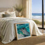 This image shows a beautiful coastal beach house or holiday home, with a placement of gentle curiosity - a little seal popping his head out of the waves in an acrylic painting as a fine art print framed against the end of the bed, while watching waves roll into the shoreline just outside the patio door. This mock up is a showcase for the print itself and does not show the print to scale, sizes are approximate and images are for representation only. Designed and made by HLSdesigner, Hannah Singleton 