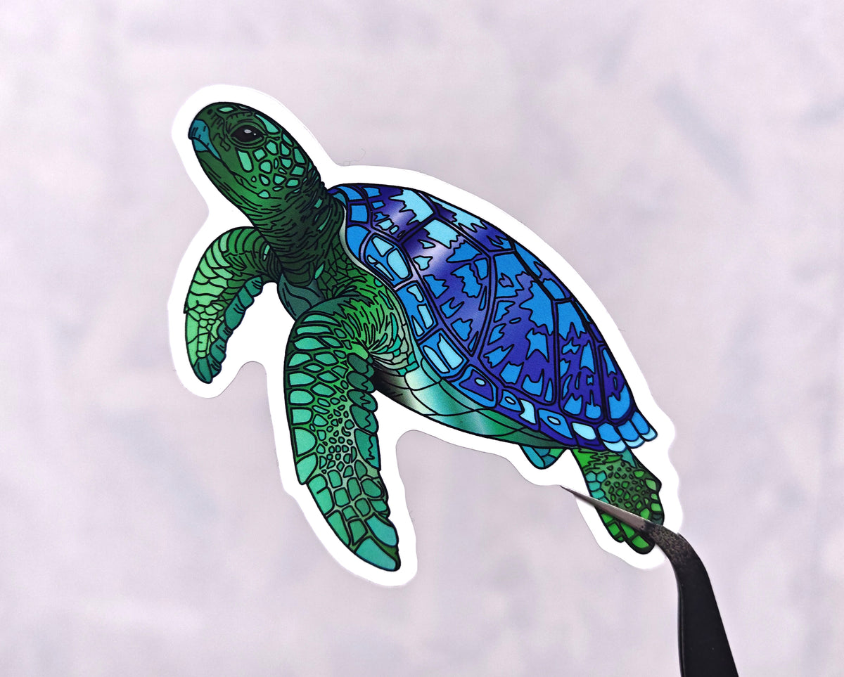 green and blue sea turtle illustration made into a die cut vinyl sticker held by tweezers against a white background