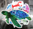 green and blue sea turtle sticker raised in the foreground with various stickers in the background blurred 