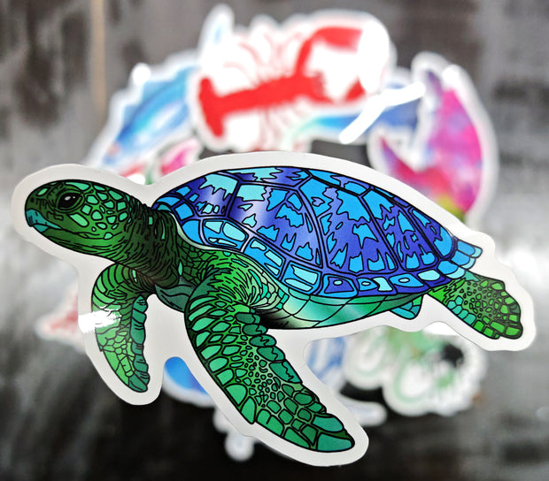 green and blue sea turtle sticker raised in the foreground with various stickers in the background blurred 