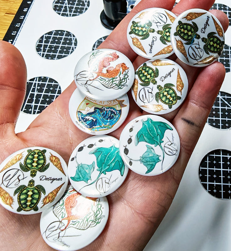 Hand holding various small round pin badges with different designs on a patterned surface.