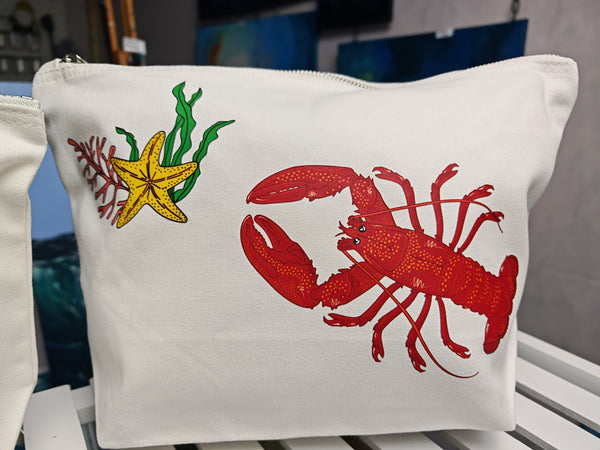 red lobster illustration by hlsdesigner printed and pressed in house onto beautiful cosmetic accessory bags, this one features the large bag with the larger lobster and starfish bundle close up on a white shelf and is complete with a silver metal zip.