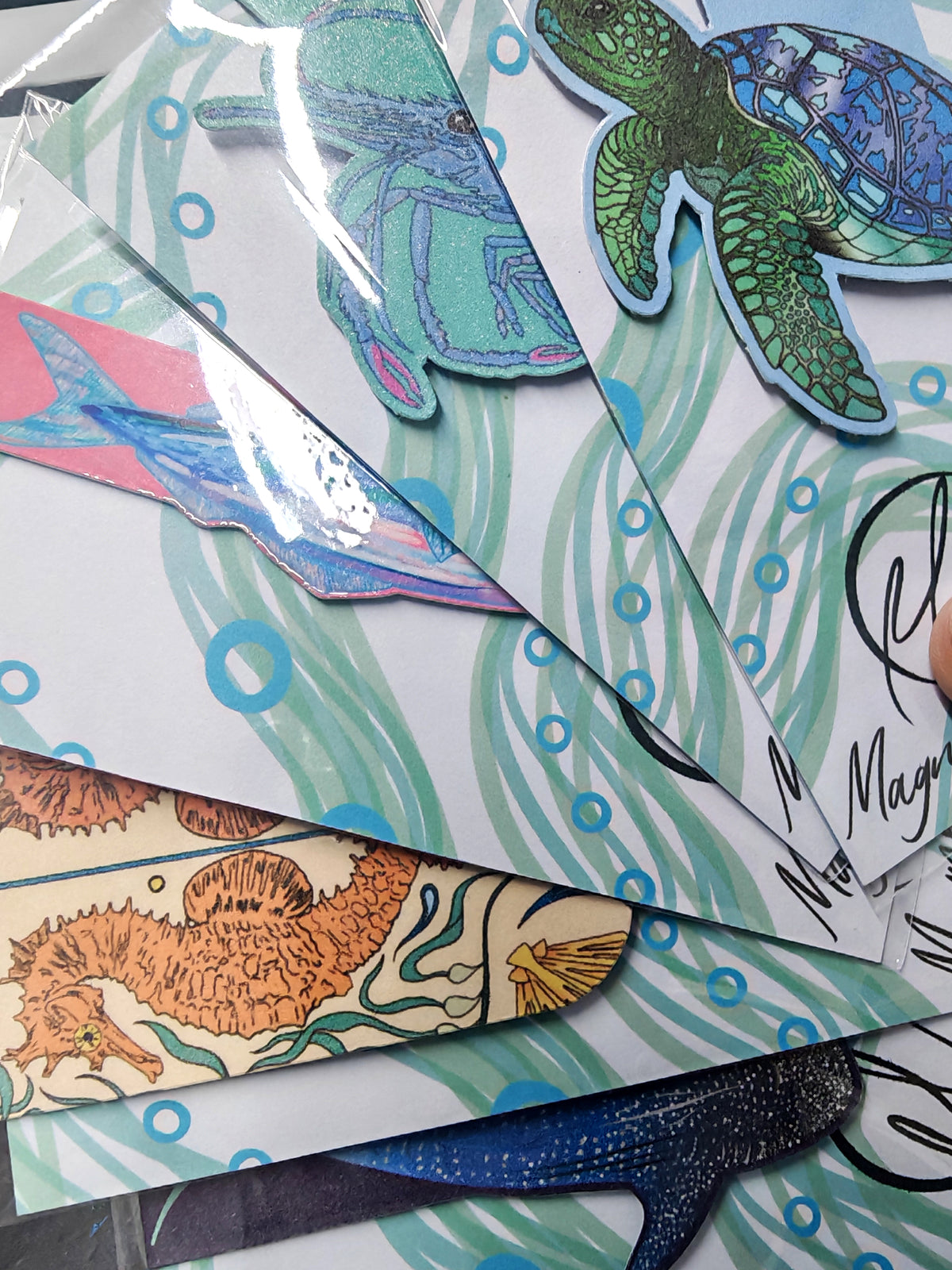 close up photo of handmade magnetic bookmarks designed and made by hand by HLSdesigner, finished with backing card in a swirled seaweed design all piled together