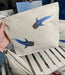 medium whale shark cosmetic bag, off white cotton canvas accessory bag with metal zip, holding in the photo for size comparison with ocean themed artwork in the background. whale shark illustration fading from blue to green with white spots pressed onto the bag, this bag features two small illustrations of the sharks swimming around the bag with the small and large bags in the background