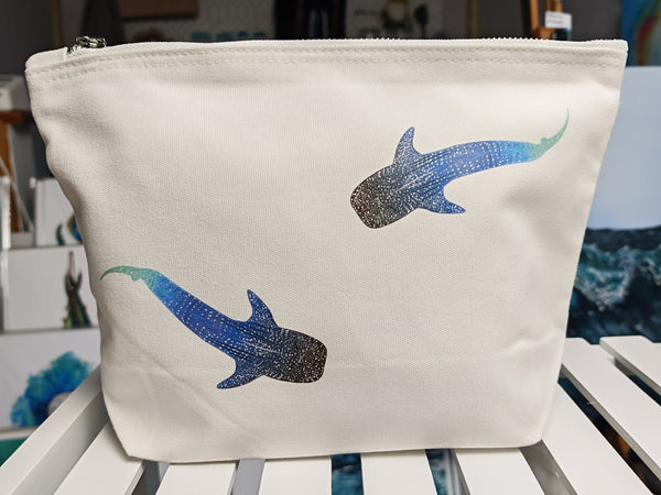 medium whale shark cosmetic bag, off white cotton canvas accessory bag with metal zip, with ocean themed artwork in the background. whale shark illustration fading from blue to green with white spots pressed onto the bag, this features two small whale sharks swimming around the bag