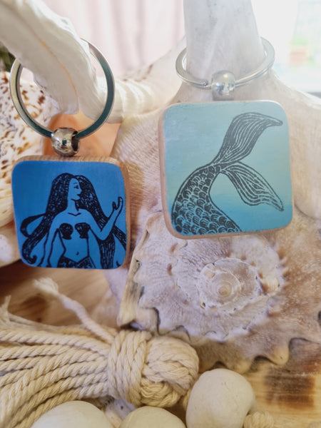 Two square hand painted keyrings with mermaid designs on a shell background