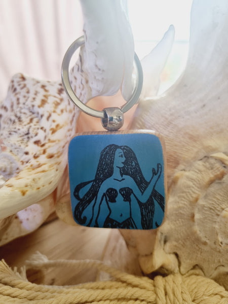 Blue square with a black silhouette of a mermaid, surrounded by seashells and rope.