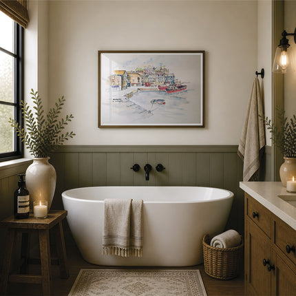 A framed watercolor painting of a harbor scene hangs on a beige wall above a white freestanding bathtub in a styled bathroom with wood wainscoting, a window, candles, towels, and a vanity. The picture in the frame is a reproduction print of an original watercolour painting by Robert singleton and produced exclusively by HLSdesigner - this is a print featuring mevagissey - a beautiful coastal town in the heart of Cornwall 