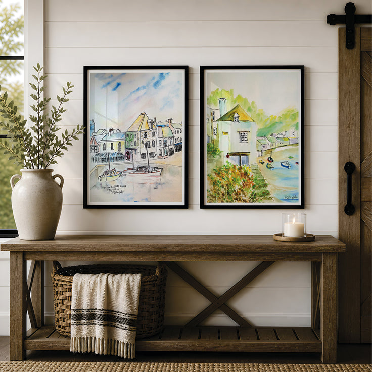 Two framed watercolour landscape prints of the old customs house in Padstow and the old watch house in Polperro - located in Cornwall - serene paintings of beautiful coastal villages in Cornwall. Hang on a white shiplap wall above a rustic wooden bench. The left print shows a coastal village with boats, and the right print shows a lakeside cottage. Originally painted by Robert Singleton - contemporary and minimalist artist from Newquay - Reproduced exclusively in honour by HLSdesigner