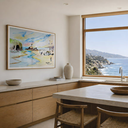 A framed coastal landscape painting hangs on a light beige wall in a modern kitchen with wood cabinetry, a stone countertop, and a large window overlooking the ocean. This is Perranporth beach. A watercolour study depicting the essence of what is perranporth and the beach goers enjoying it. A coastal seascape beach scene originally painted in watercolour by artist Robert singleton showcasing his minimalist contemporary work. Reproduced exclusively by Hannah singleton at HLSdesigner.