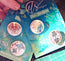 Two packs of pin badges with ocean-themed designs on a cutting mat.
