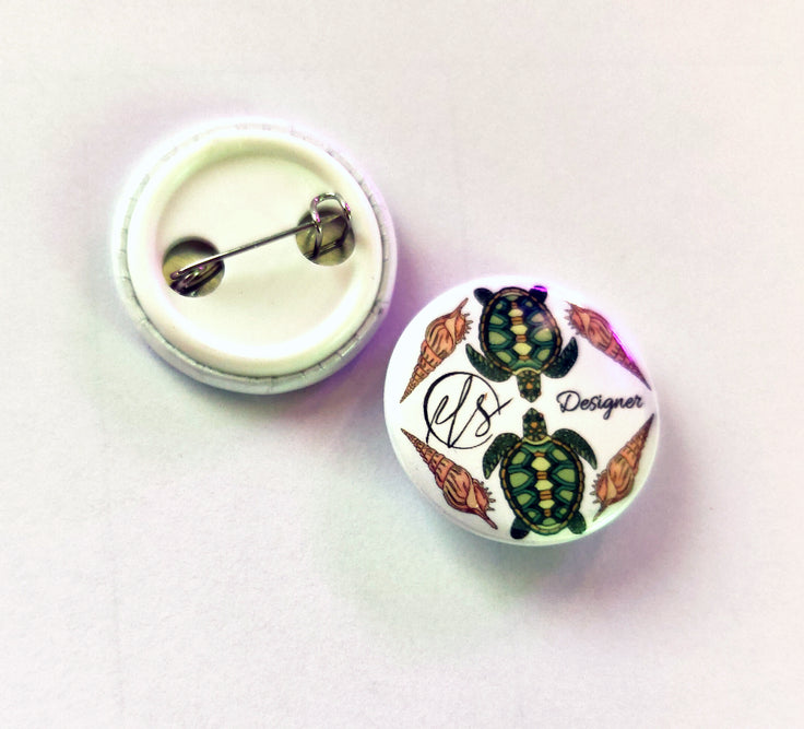 Button badge with turtle design and HLS 'Designer' text on a white background with turtles and shells, handmade and designed in house
