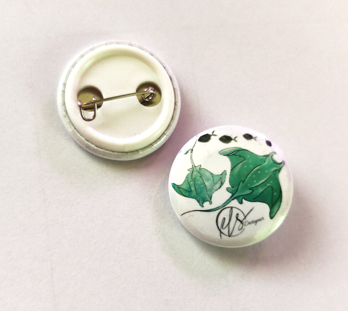 Button badge with greeny blue manta rays design on a white background