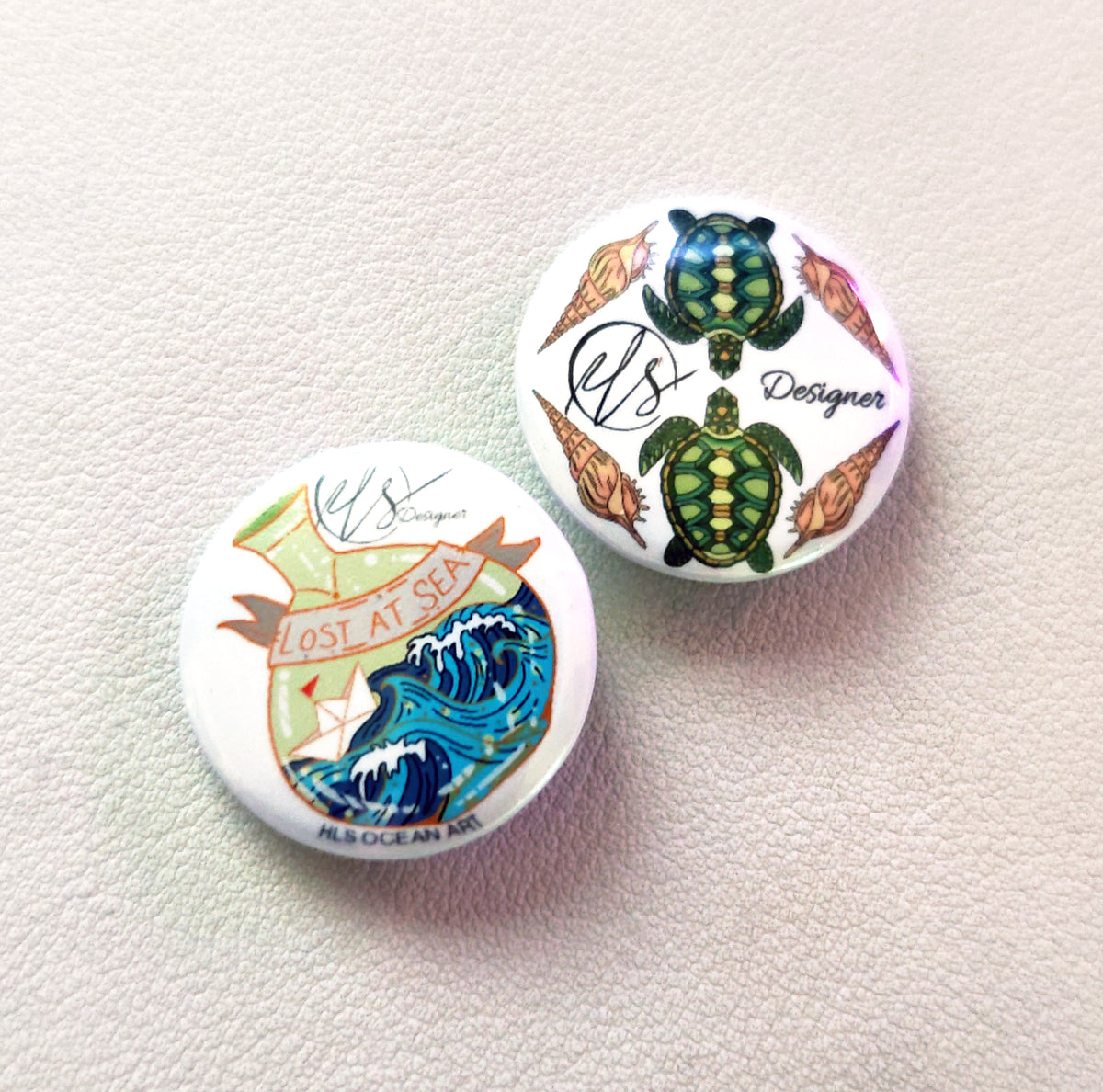 Two button pin badges with turtle designs on a light background with lost at sea message in a bottle illustration