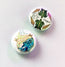 two circular pin badges collectable as a set of two, one with a message in a bottle design on and one with turtles and shells with the HLSdesigner logo, designed and made in house