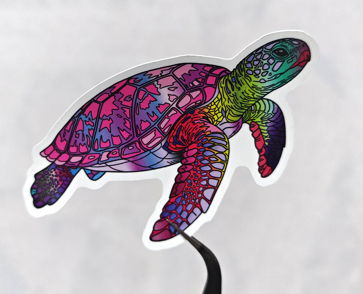 pink, purple, green and yellow hues in a pink overall sea turtle illustration made into a die cut vinyl sticker being held with tweezers against a white background