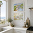 Two framed watercolor landscape and village art prints hanging on a white kitchen wall above a countertop with plants and a bowl of limes. These fine art prints are of Polperro in colour and Mawganporth beach - two coastal townscapes by contemporary and minimal artist Robert Singleton - reproduced excusively by HLSdesigner 
