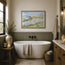 A framed landscape watercolour painting hangs on a beige wall above a white freestanding bathtub in a rustic bathroom setting with wood wainscoting, a stone countertop, and decorative towels. This is a reproduction print of an original watercolour painting by Robert Singleton - A contemporary study of Porth beach in Newquay - inspired by the picturesque natural scapes of Cornwall. Modern and abstract all at once. A beautiful representation of life in Cornwall. Reproduced exclusively by HLSdesigner