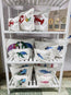 designed and printed in house at hlsdesigner, view the full range of cosmetic accessory bags in all sizes, small, medium and large. set on a white shelving unit complete with a QR coded social media poster directing to facebook, tiktok and online. on the top shelf is a lobster collection complete with a starfish and seaweed. On the middle shelf is the turtle collection and the whale shark collection, and on the bottom shelf is an inky squid collection and a colourful pink and blue sardine collection.