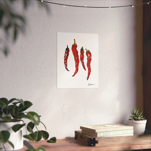 Framed artwork of red chili peppers on a wall above a wooden table with plants.