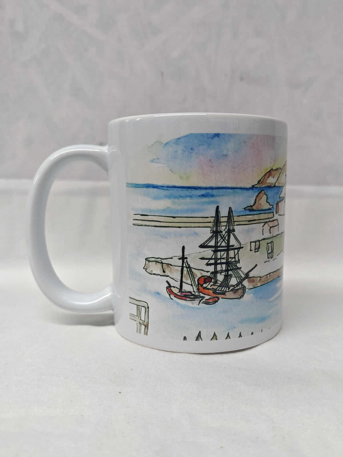 A ceramic mug with a full wrap around print of Charlestown harbour showcasing the fishing village overlooking the tall ships that moor in the historic quay. This image is on the side of the print focusing on the ocean in the background and the quay entrance where the tall ships settle against the quay wall. Painted in watercolour by Cornwall artist R Singleton and reproduced in tribute by HLSdesigner