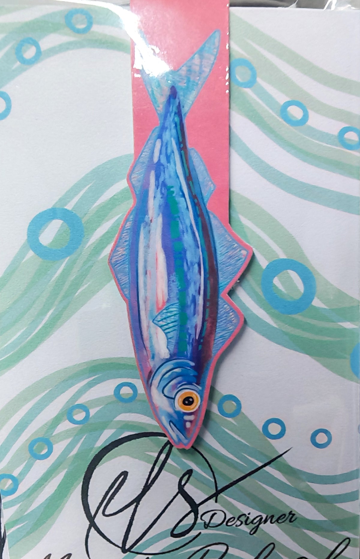 sardine illustration handmade magnetic bookmark on a pink background, cardstock and magnets encase the page holding the place of reading. on a seaweed inspired swirled backing card