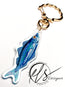 watercolour inspired sardine illustration with blues and greens throughout and a bold orange fish eye. Finished in clear acrylic and shaped to the fish with a metal seashell shaped keychain clasp for ocean decoration, image taken on a white background with the HLSdesigner logo in the corner, coastal inspired art and home décor 