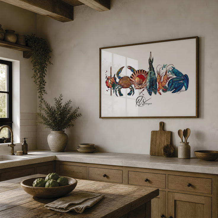 A framed art print featuring a colorful illustration of crabs and a fish on a white background, hanging on a beige wall in a rustic kitchen with wooden cabinets, a stone countertop, and a wooden island. The art on the wall is a piece by Hannah Singleton, a contemporary fine artist inspired by the ocean from Cornwall. This is the seafood platter print, featuring a prawn skewer, blue sand crab, scallop shell, mackerel, langoustines and mussels all layered together in a row ready for prep. at HLSdesigner