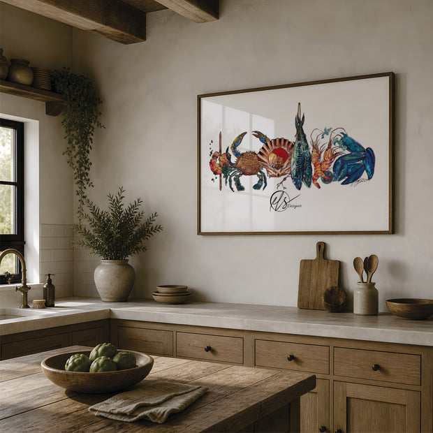 A framed art print featuring a colorful illustration of crabs and a fish on a white background, hanging on a beige wall in a rustic kitchen with wooden cabinets, a stone countertop, and a wooden island. The art on the wall is a piece by Hannah Singleton, a contemporary fine artist inspired by the ocean from Cornwall. This is the seafood platter print, featuring a prawn skewer, blue sand crab, scallop shell, mackerel, langoustines and mussels all layered together in a row ready for prep. at HLSdesigner