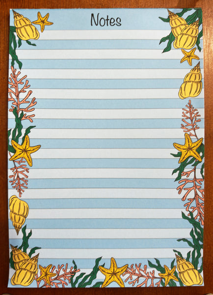 beach inspired seashell notepad, 50 tear off pages with a striped blue and white background for note taking surrounded with bright yellow and orange seashells, starfish, coral and green seaweeds handmade by HLSdesigner