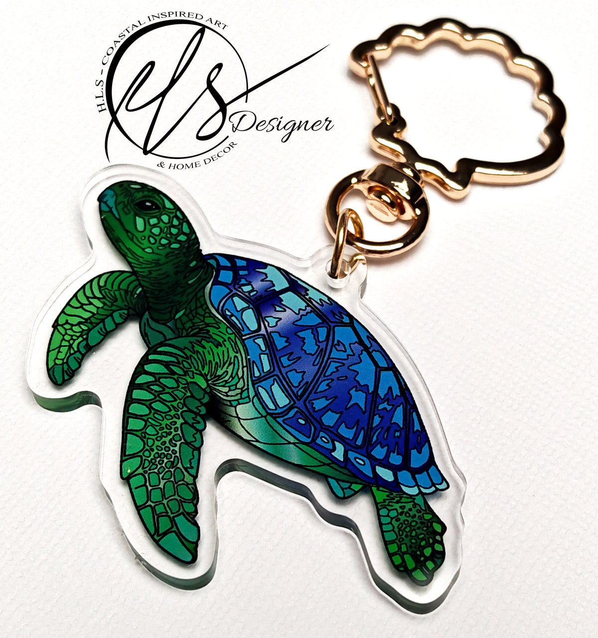 Green and blue sea turtle playful illustration printed into acrylic die cut around and finished with a gold metal seashell shaped keychain clip ring, photo is on a white background with the HLSdesigner logo which reads HLS coastal inspired art and home décor. Designed by HLSdesigner in Cornwall, make your keys, bags and accessories stand out with the ocean collection now