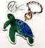 Green and blue sea turtle playful illustration printed into acrylic die cut around and finished with a gold metal seashell shaped keychain clip ring, photo is on a white background with the HLSdesigner logo which reads HLS coastal inspired art and home décor. Designed by HLSdesigner in Cornwall, make your keys, bags and accessories stand out with the ocean collection now